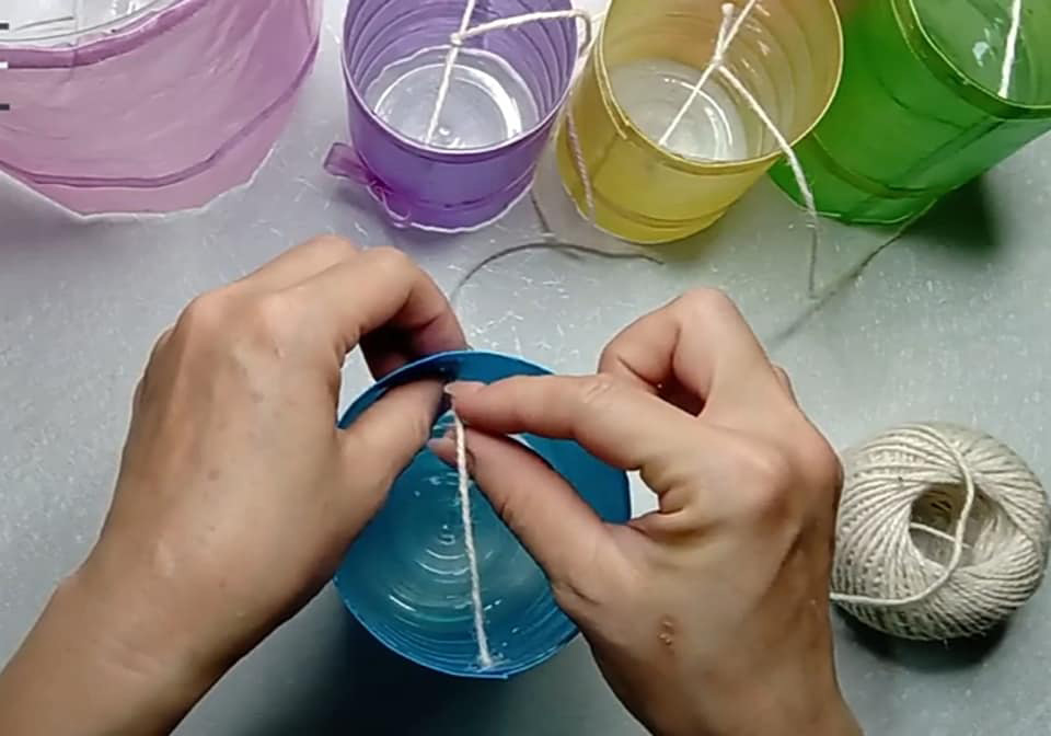 Dùng keo nến gắn hai đầu sợi dây vào hai bên thành chai, cách miệng chai khoảng 1cm rồi buộc đầu một đoạn dây vào giữa